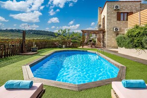 Ein Schwimmbad mit Holzterrasse, einer Pergola und Blick auf eine gebirgige Landschaft.
