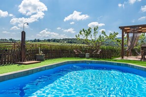Ein Schwimmbad mit Holzterrasse, einer Pergola und Blick auf eine gebirgige Landschaft.