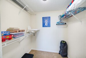 Ein kleiner, ordentlicher Raum mit einem weißen Regal mit Gesellschaftsspielen, einem weißen Stuhl, einem blauen Poster an der Wand und einer schwarzen Tasche an der Wand.