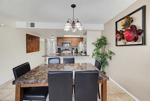 A modern kitchen with stainless steel appliances, a dining area with a marble table and leather chairs, and a decorative wall piece. - Whimsical Wonders Sweetwater Club Near Disney (Kissimmee)