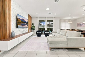 Een moderne woonkamer met een grote flatscreen televisie, een bank, een salontafel en een eethoek met stoelen.