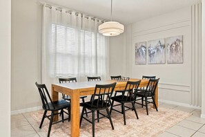 A dining room with a wooden table and black chairs, a white ceiling light, and a window with sheer curtains. - Family Dream Home Pool Arcade Slide Bed 2472 (Kissimmee)