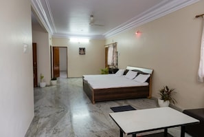 A bedroom with a bed, a table, and a ceiling fan. - The Shyam Haven (UJJAIN)