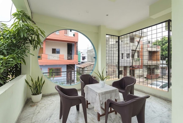 A balcony with a table and chairs, a potted plant, and a view of neighboring buildings. - The Shyam Haven (UJJAIN)