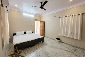A bedroom with a bed, ceiling fan, and a potted plant. - The Shyam Haven (UJJAIN)