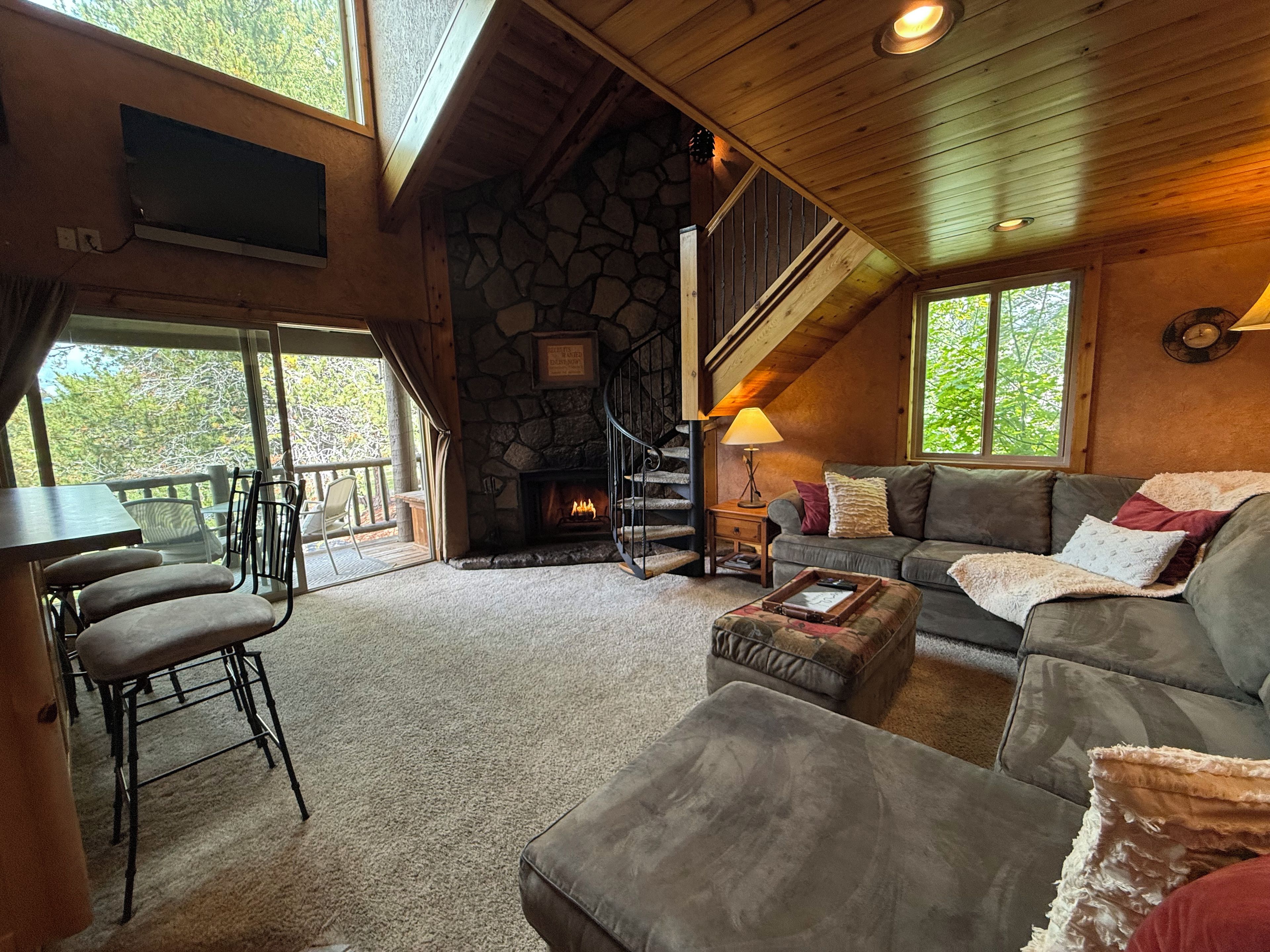 A cozy living room with a stone fireplace, a staircase, a sofa, and a dining area with chairs.
