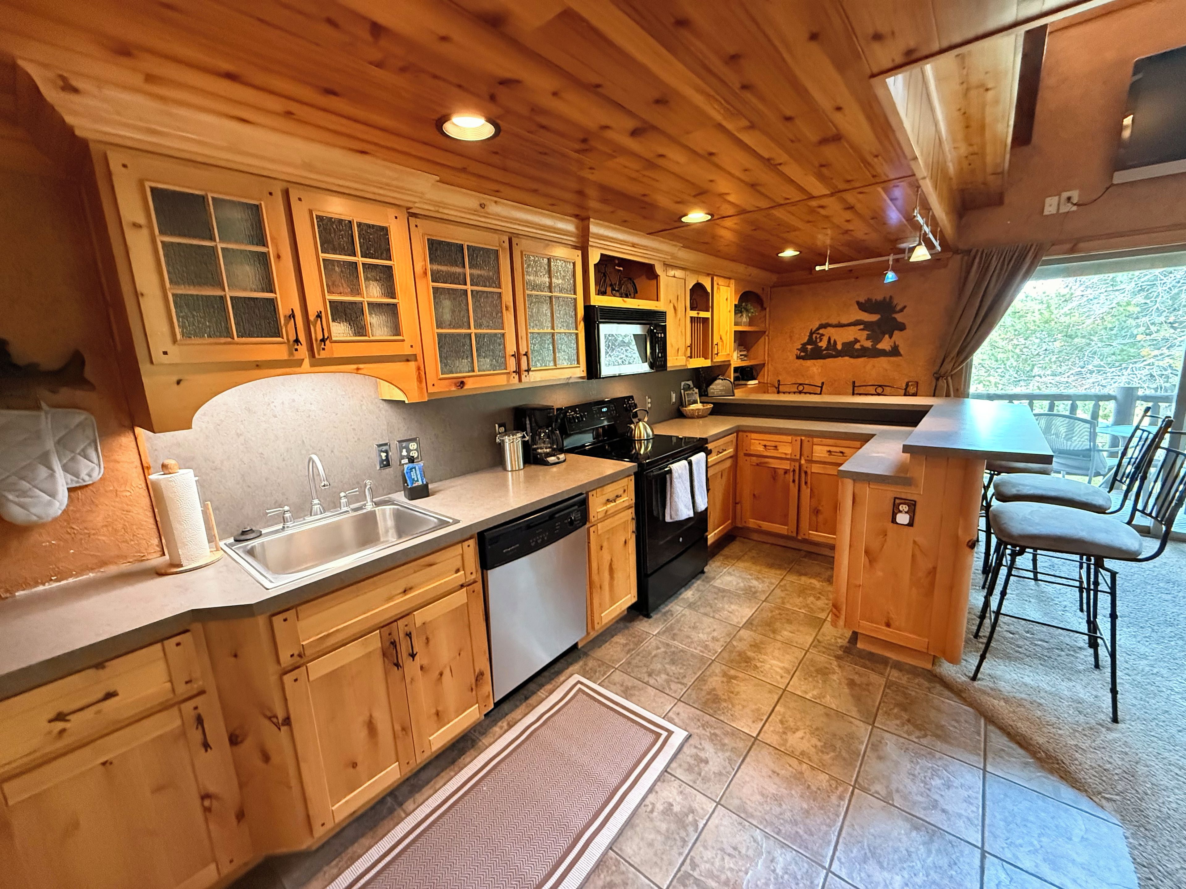 A wooden cabin kitchen with a sink, stove, and dining area.