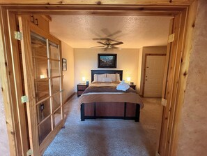 Ein Hotelzimmer mit Bett, Deckenventilator, Gemälde und Tür.