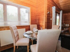 A wooden interior with a round glass table set for two, two upholstered chairs, and a window with blinds. - 89 Ambleside (Windermere)