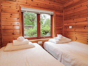 A room with wooden walls and a window overlooking greenery. There are two beds with white linens and towels. - 89 Ambleside (Windermere)