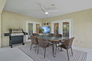 An outdoor patio with a round table, wicker chairs, a grill, and a ceiling fan. - Shore Thing at Vanderbilt – Naples Park Retreat, Bike to the Beach! (Naples)