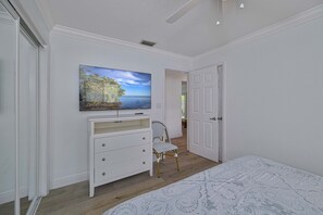 A bedroom with a bed, a dresser, a chair, and a painting on the wall. - Shore Thing at Vanderbilt – Naples Park Retreat, Bike to the Beach! (Naples)