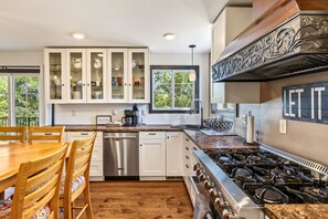 Una cocina moderna con armarios blancos, un lavavajillas de acero inoxidable, una estufa a gas y un comedor con sillas de madera.