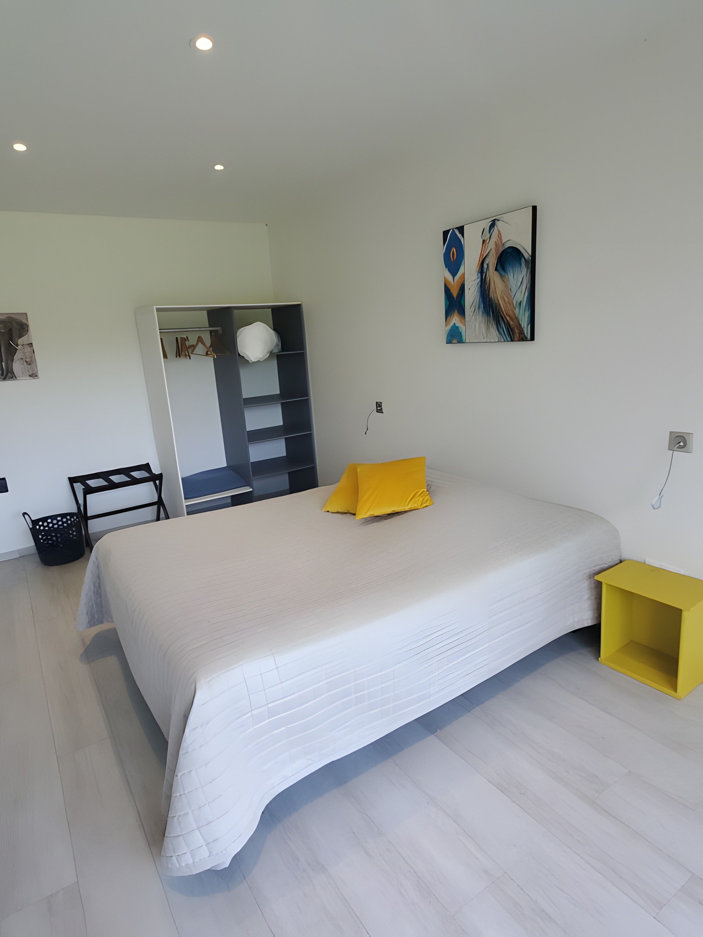 A modern bedroom with a large bed, a wardrobe, a bedside table, and a wall-mounted artwork.