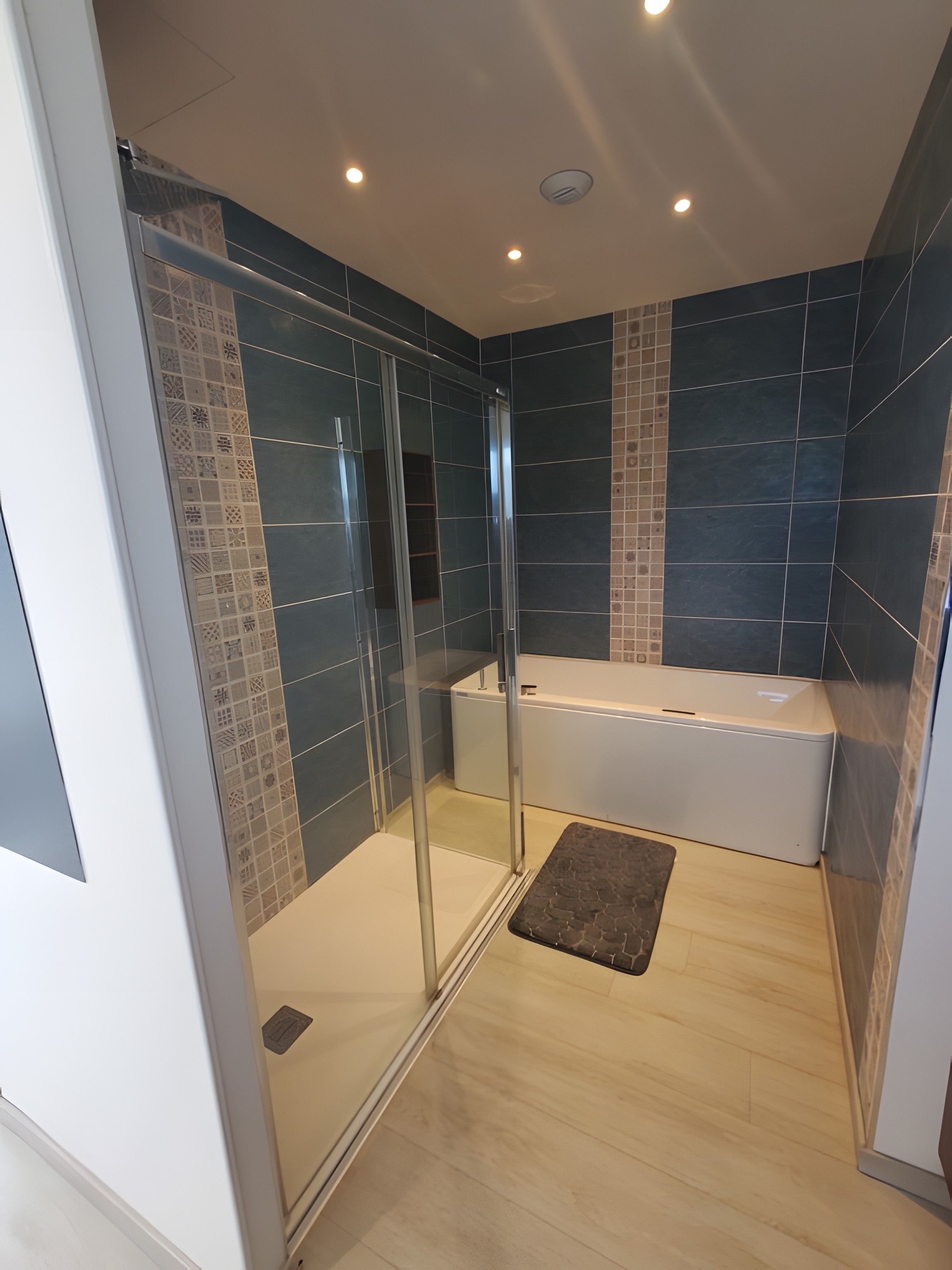 Une salle de bain moderne avec une douche à parois de verre, une baignoire et des murs recouverts de carreaux bleu foncé.