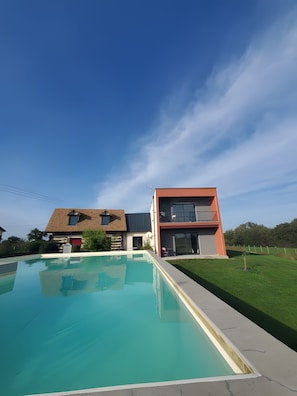 Una casa moderna con piscina, balcón y césped bien cuidado.