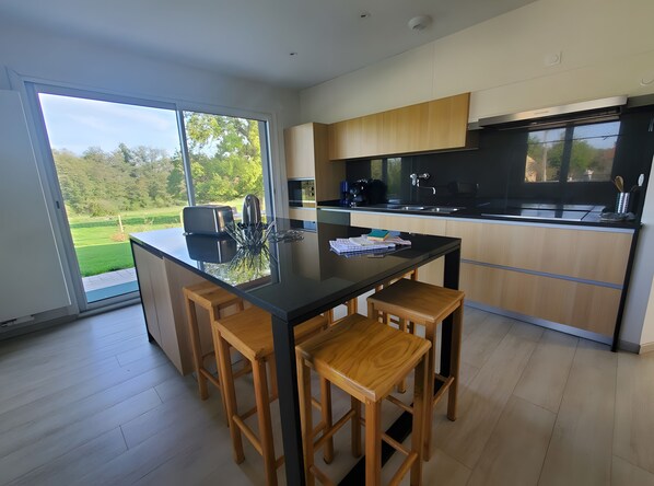 Una cocina moderna con una isla grande, taburetes de madera y vistas a un paisaje verde a través de una puerta corrediza de vidrio.