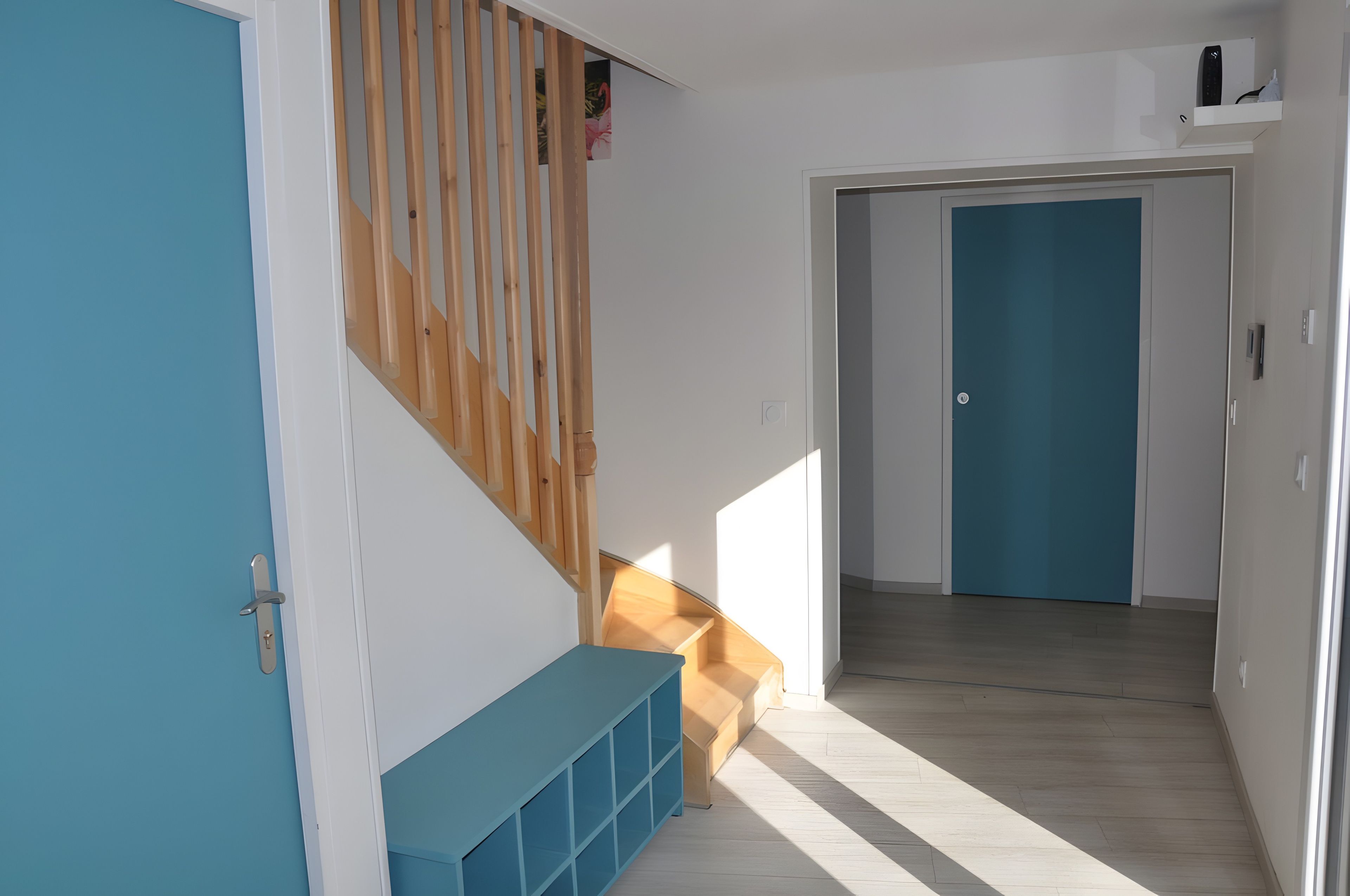 A hallway with a blue door, a wooden staircase, and a blue bench.