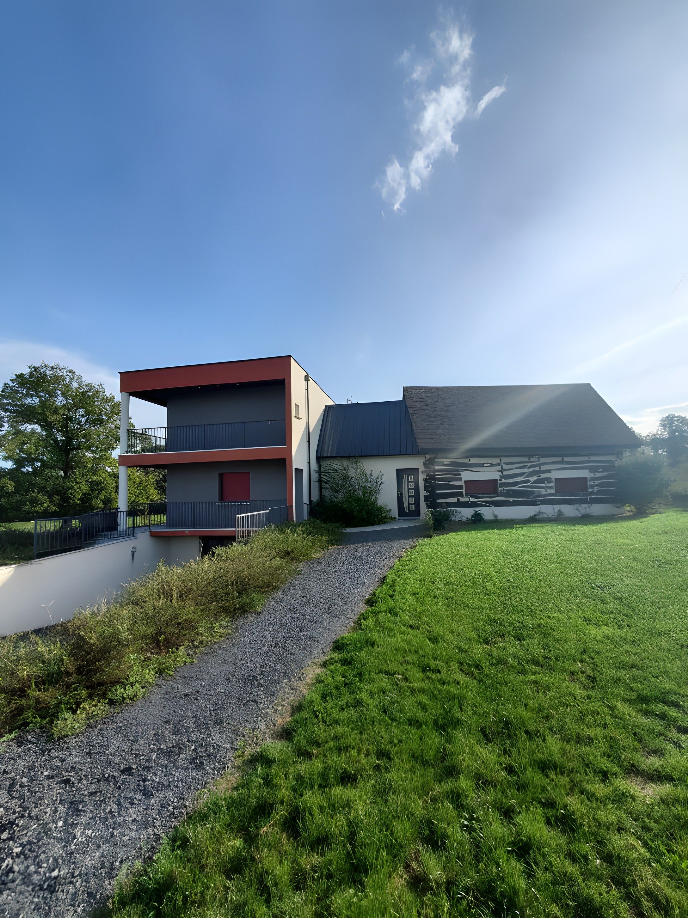 A modern two-story house with a red and grey facade, a gravel driveway, and a grassy lawn.