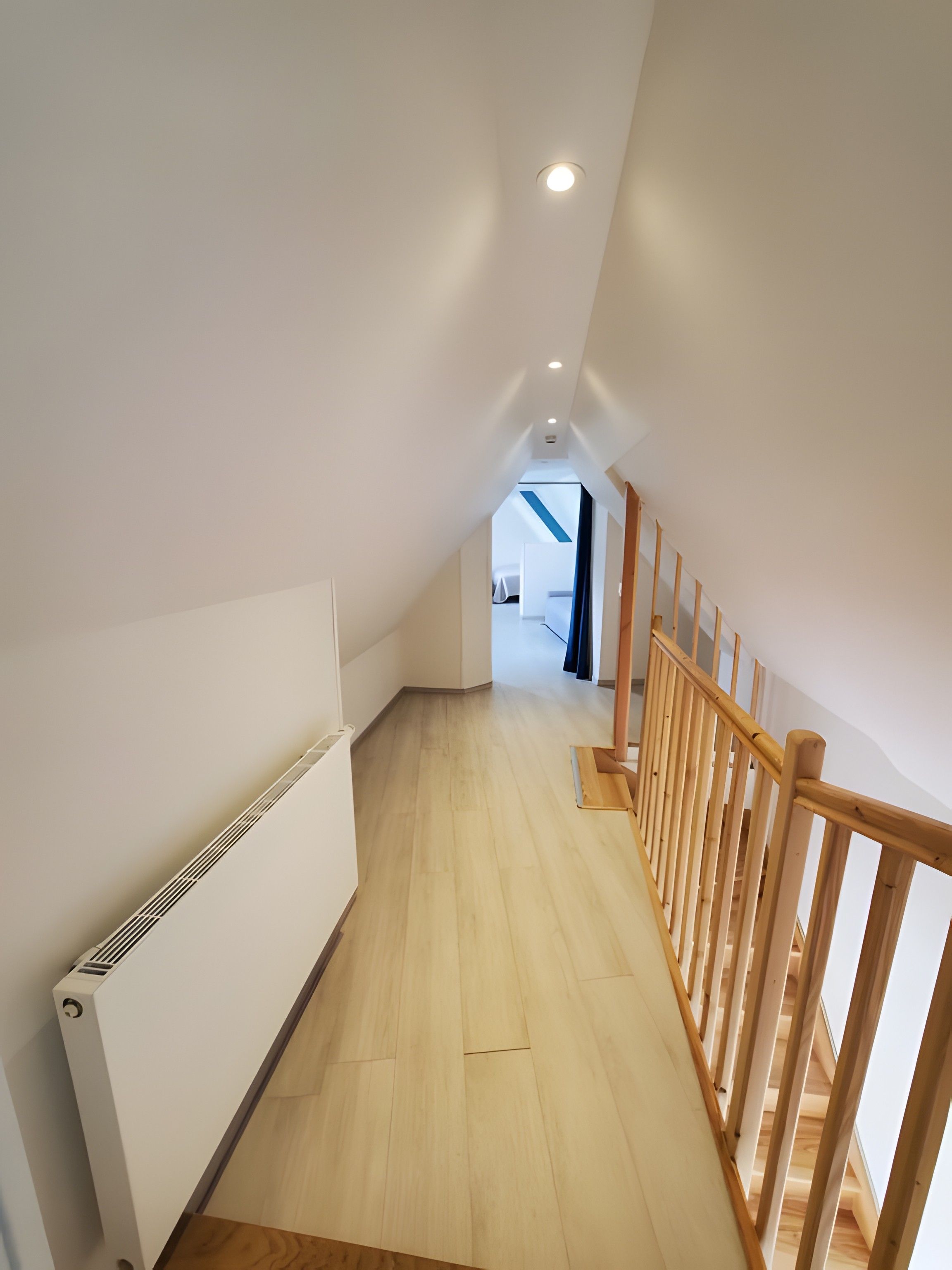 A modern interior with a wooden staircase, white walls, and a visible radiator.