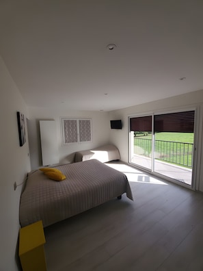 Un dormitorio con cama, televisión y balcón con vista a un paisaje verde.