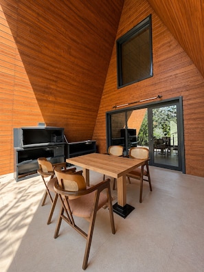 Een modern interieur met een houten schuine daklijn, een eethoek met tafel en stoelen, een inbouwmeubel en een grote schuifdeur naar een buitenruimte.