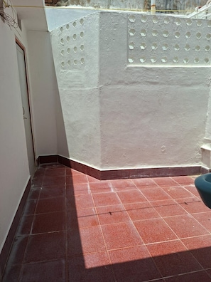 Una esquina de una habitación con piso de baldosas rojas, una pared blanca con textura y una puerta.