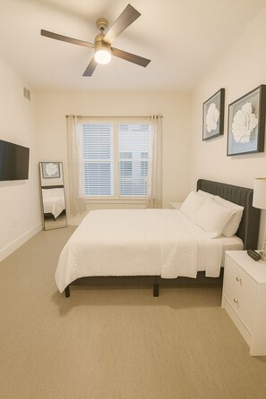A bedroom with a bed, a nightstand, a bedside table, a ceiling fan, and a window with blinds. - 2 Bedrooms • 2 Full Bathrooms • King + Queen Beds • Prime Frisco Location (Frisco)