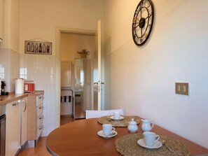 A modern kitchen with white cabinets, a wooden dining table with white cups and saucers, and a decorative wall clock. - The Washington Studio Apartment - with balcony (Milano)
