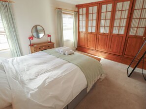 A bedroom with a large bed, a wooden wardrobe, a mirror, and a window with curtains. - Seaglass Cottage (Hull)