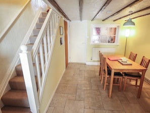 A staircase with a white railing leading to a door, a dining table with chairs, and a radiator on the wall. - Seaglass Cottage (Hull)