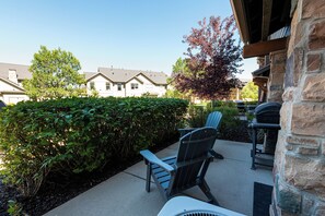 Eine Terrasse mit zwei Adirondack-Stühlen, einem Grill und einer Steinmauer.