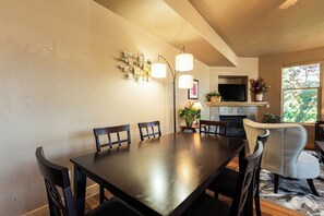 A dining area with a dark wooden table and chairs, a wall-mounted light fixture, and a fireplace with a television. - 2BR Park City townhome in Kimball Junction with mountain views. (Park City)