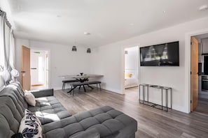 Ein modernes Wohnzimmer mit einem grauen Sofa, einem Esstisch und einem an der Wand befestigten Flachbildfernseher.