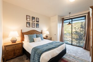 Une chambre à coucher comprenant un lit, des tables de chevet, une fenêtre avec vue et des œuvres d’art murales.