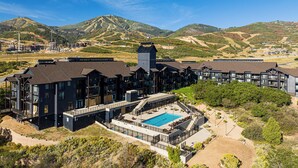 Un hotel moderno con varias edificaciones, piscina y montañas al fondo.