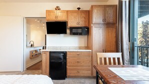 Una cocina compacta con armarios de madera, un refrigerador negro, un microondas y un comedor con mesa y silla.