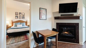 Quarto de hotel com uma cama, televisão sobre a lareira e área de jantar com mesa e cadeiras.