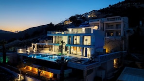 Uma casa moderna de dois andares com piscina, área de estar externa e vista para as colinas ao redor.
