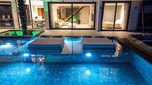 Uma área de piscina moderna ao ar livre com duas espreguiçadeiras e um alpendre envidraçado.