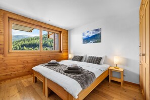 A bedroom with a large window, a bed with grey and white bedding, a small bedside table with a lamp, and a framed picture on the wall. - Echo 8 - Sleeps 7 - Magnificent Luxury Penthouse (Haute-Nendaz)