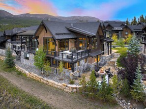 Un chalet à étages doté d’une façade en pierre, de balcons et d’un espace aménagé autour d’un foyer.