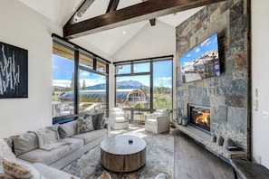 A spacious living room with a fireplace, large windows, and a view of mountains. - 🏆 Falcon Haus MidStation Gondola | 2 Hot Tubs | Sleeps 10 (Breckenridge)