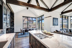 Une cuisine moderne dotée d’un grand îlot central, de poutres en bois et de grandes fenêtres offrant une vue sur un paysage montagneux.