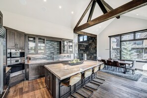 A modern kitchen with a large island, dark cabinetry, and a stone backsplash. - 🏆 Falcon Haus MidStation Gondola | 2 Hot Tubs | Sleeps 10 (Breckenridge)