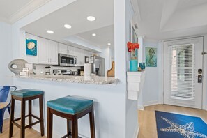 A modern kitchen with white cabinets, stainless steel appliances, and a marble countertop. There are two bar stools with teal cushions. - Heron Walk 8986 Golf Cart, Pool, Sleeps 6 (Miramar Beach)