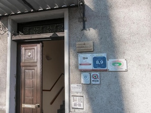 Entrada de un edificio con puerta de madera, una escalera y varias placas en la pared.