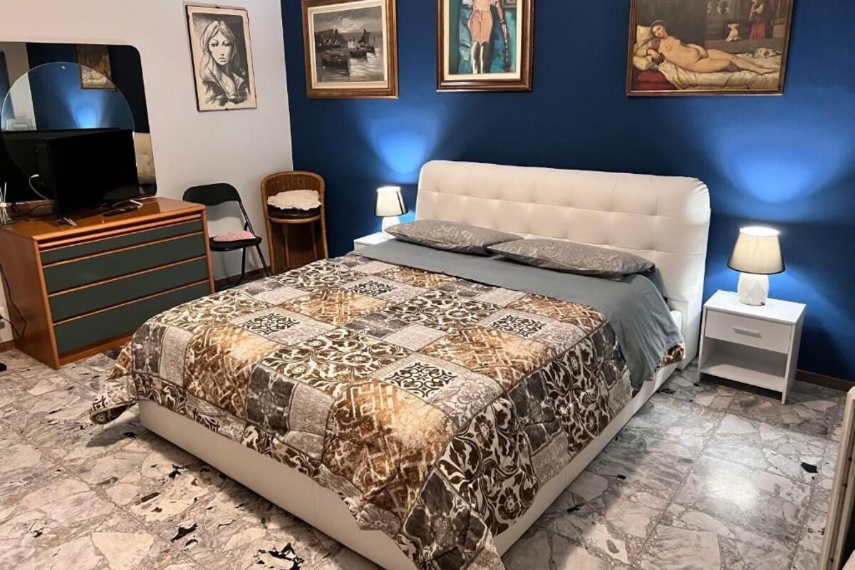 A bedroom with a bed, a television, a desk, and chairs.