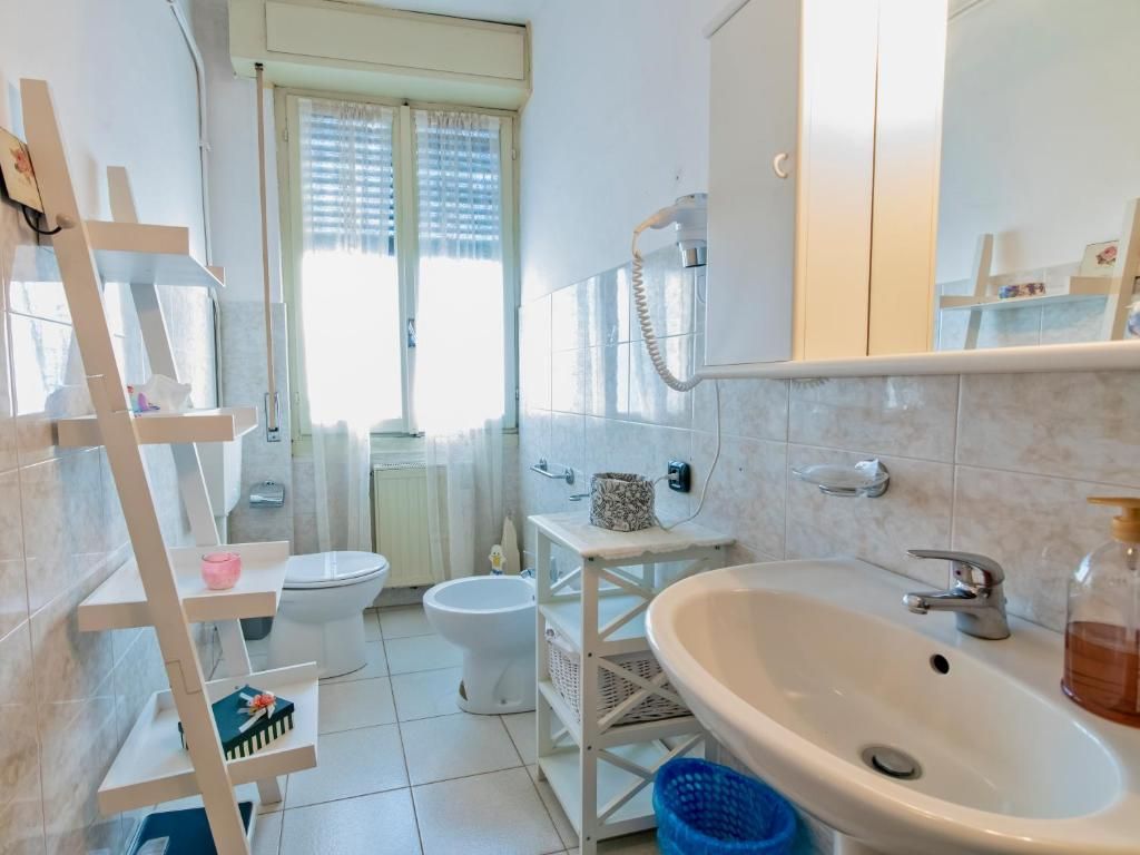 Un baño con lavamanos blanco, inodoro, bidé y un estante con artículos de aseo.