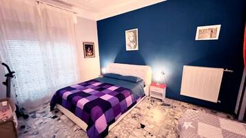 A bedroom with a bed, a nightstand, a radiator, and a window with curtains.